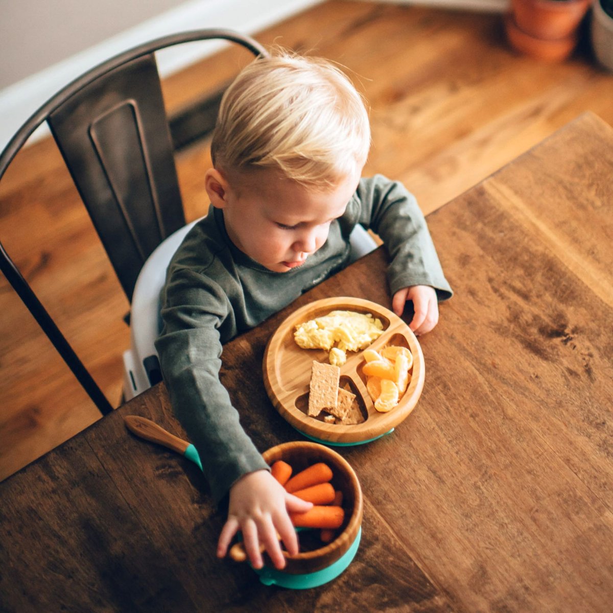A child at the family table with a bamboo divided plate, matching bowl and green silicone suction bases.
