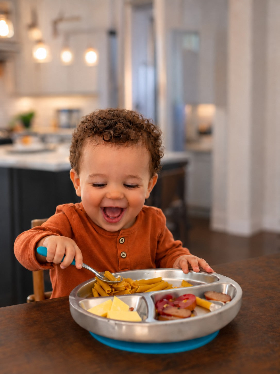 Smiling child enjoying pasta from an Avanchy divided stainless steel plate with a blue suction base.